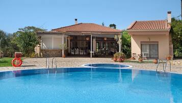 A swimming pool with a lifebuoy, a covered patio area, and a small building with a tiled roof.