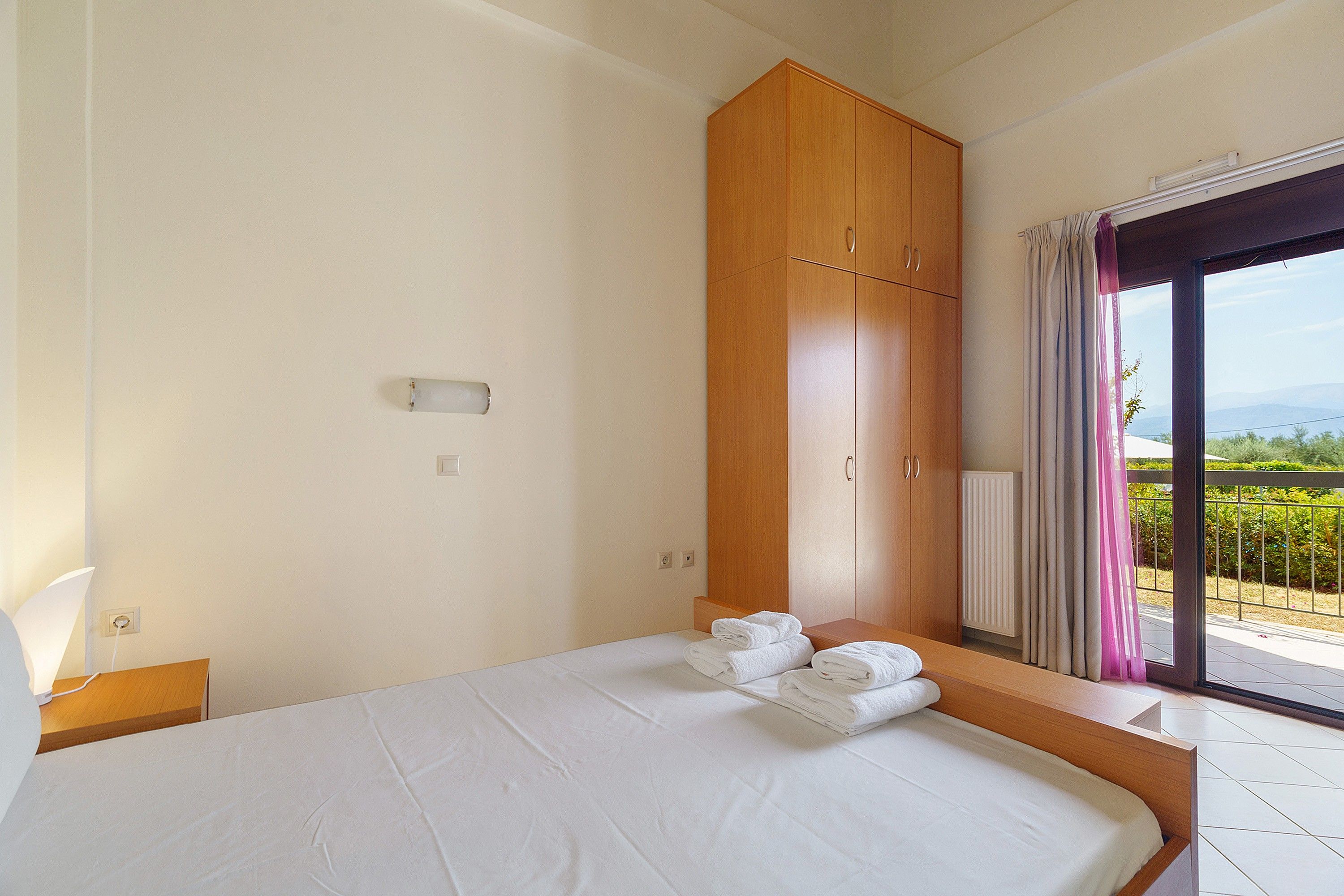 Habitación de hotel con cama, armario de madera, ventana con cortinas y vistas al exterior.