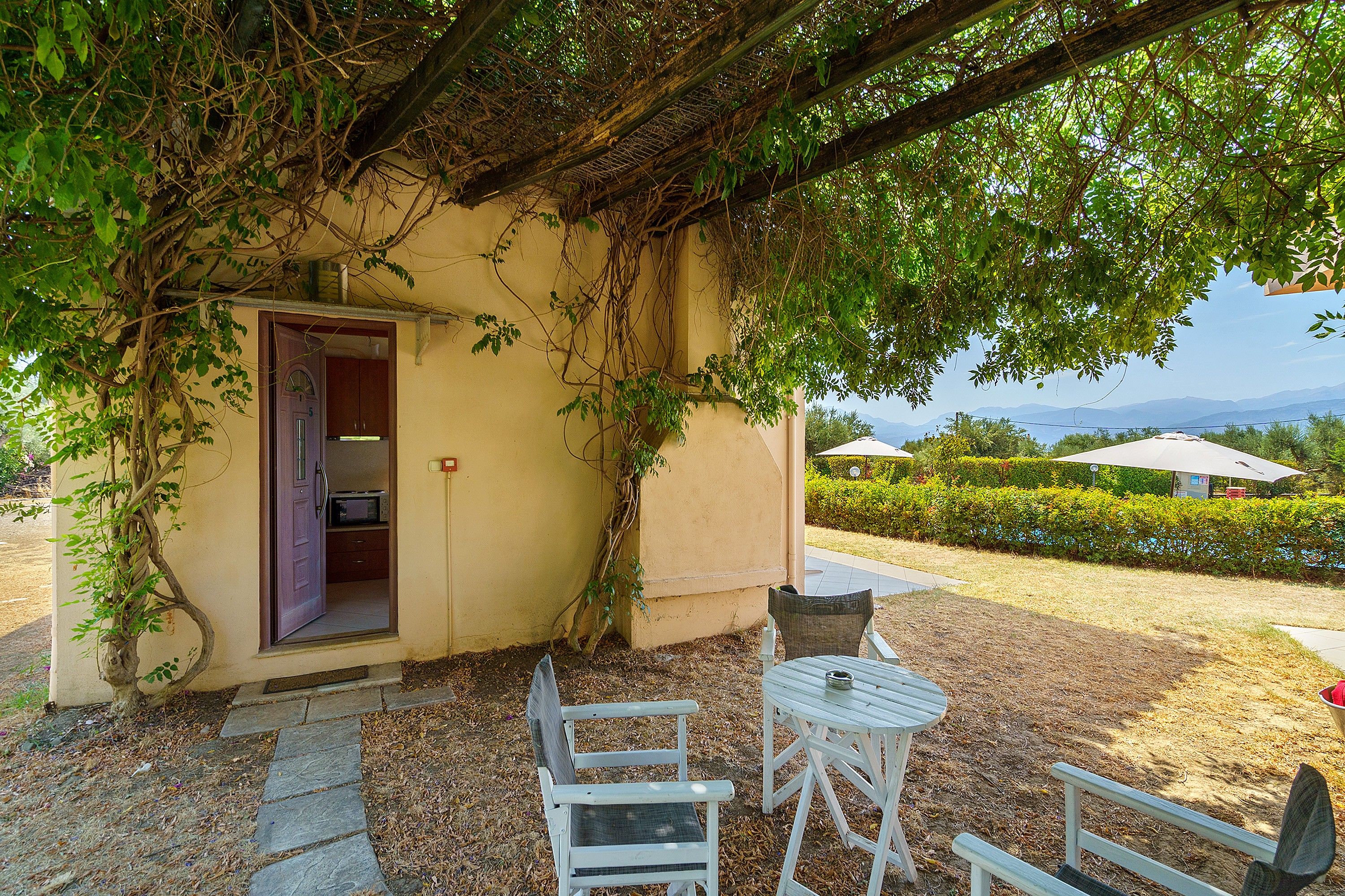 Un espace extérieur abrité, avec une table et des chaises, une porte donnant sur une pièce et une vue sur le paysage.