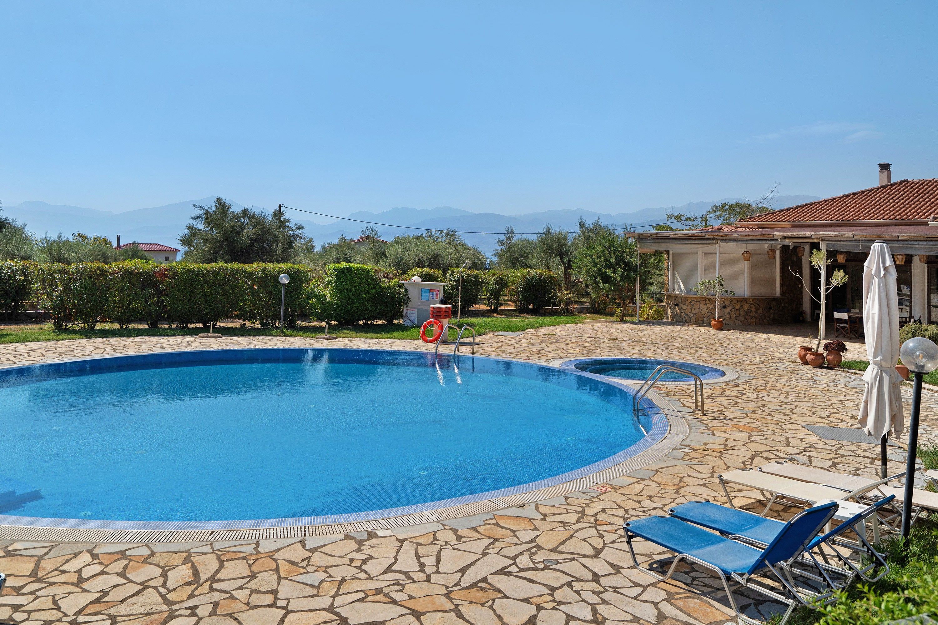A swimming pool with a stone deck, lounge chairs, and a view of mountains.