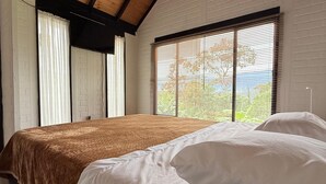 A bedroom with a large bed, wooden beams, white walls, and a window with blinds. - Cozy La Chorrera Cabin Surrounded by Nature with a View of the Mountains (Venecia)