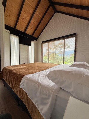 Ein Schlafzimmer mit einem großen Bett, Holzbalken, weißen Wänden und einem Fenster mit Jalousien.