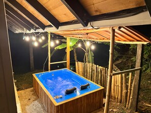 A hot tub under a wooden structure with a bamboo fence and string lights.
