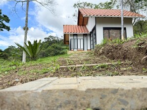 A modern house with a red-tiled roof, a stone pathway leading to the entrance, and a lush green landscape with trees and plants.