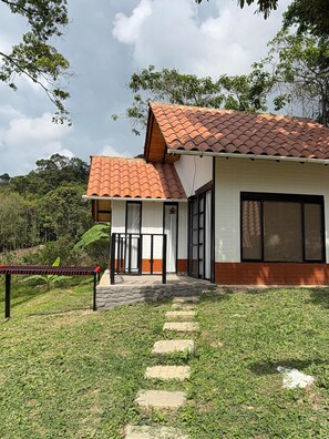 A building with a red-tiled roof, white walls, and a brick base. It features a covered entrance with a glass door and a small porch area.
