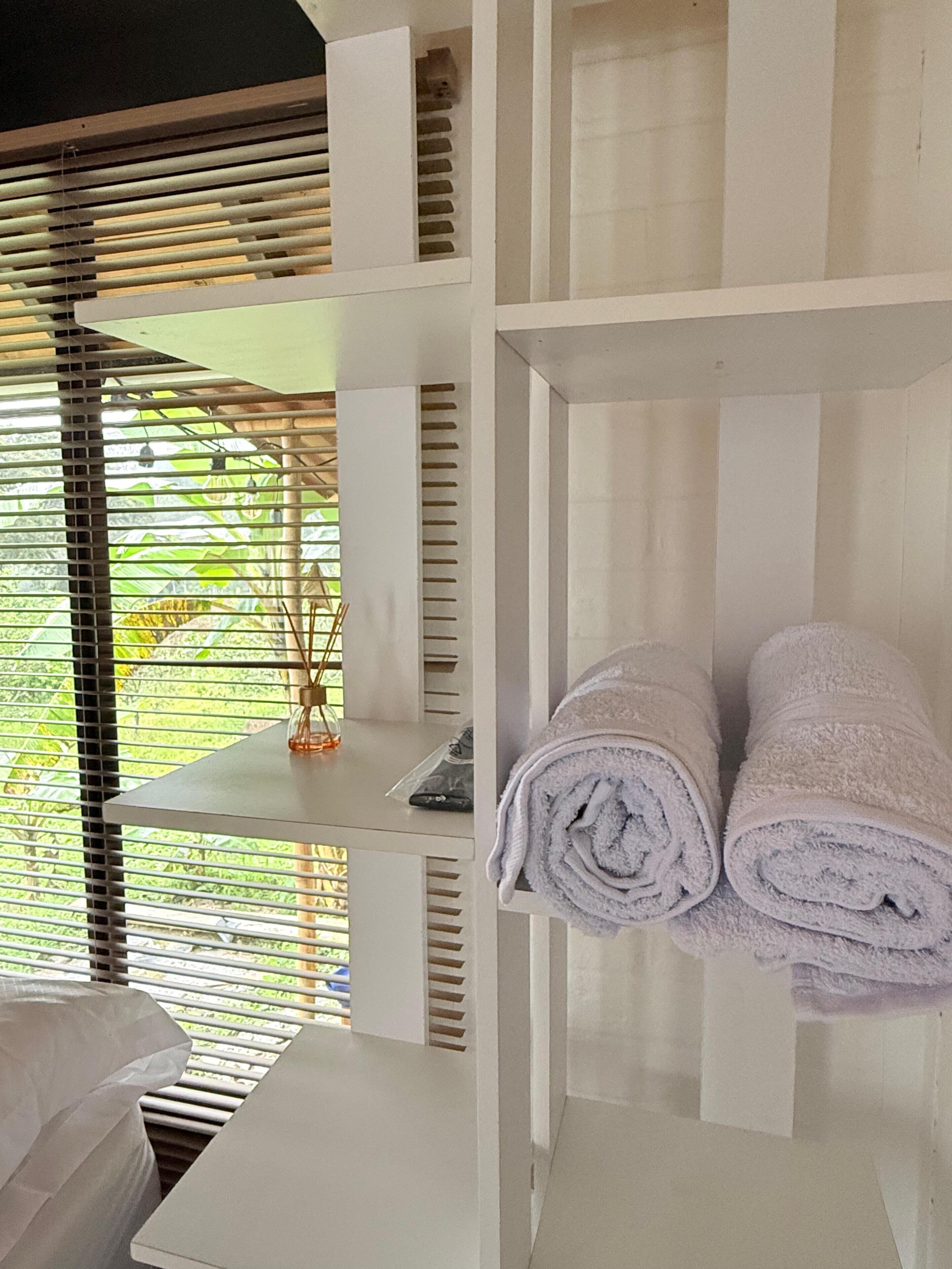 Une chambre avec un lit, une table et une étagère où sont pliés des serviettes.