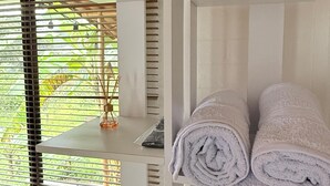 A room with a bed, a table, and a shelf with rolled towels. - Cozy La Chorrera Cabin Surrounded by Nature with a View of the Mountains (Venecia)