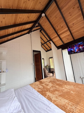 A room with a bed, a wooden ceiling, a brick wall, and a television.