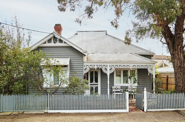A two-story house with a grey facade, white trim, and a decorative porch with white railings. - The Merri Classic Victorian Home by Walking Trails (Northcote)