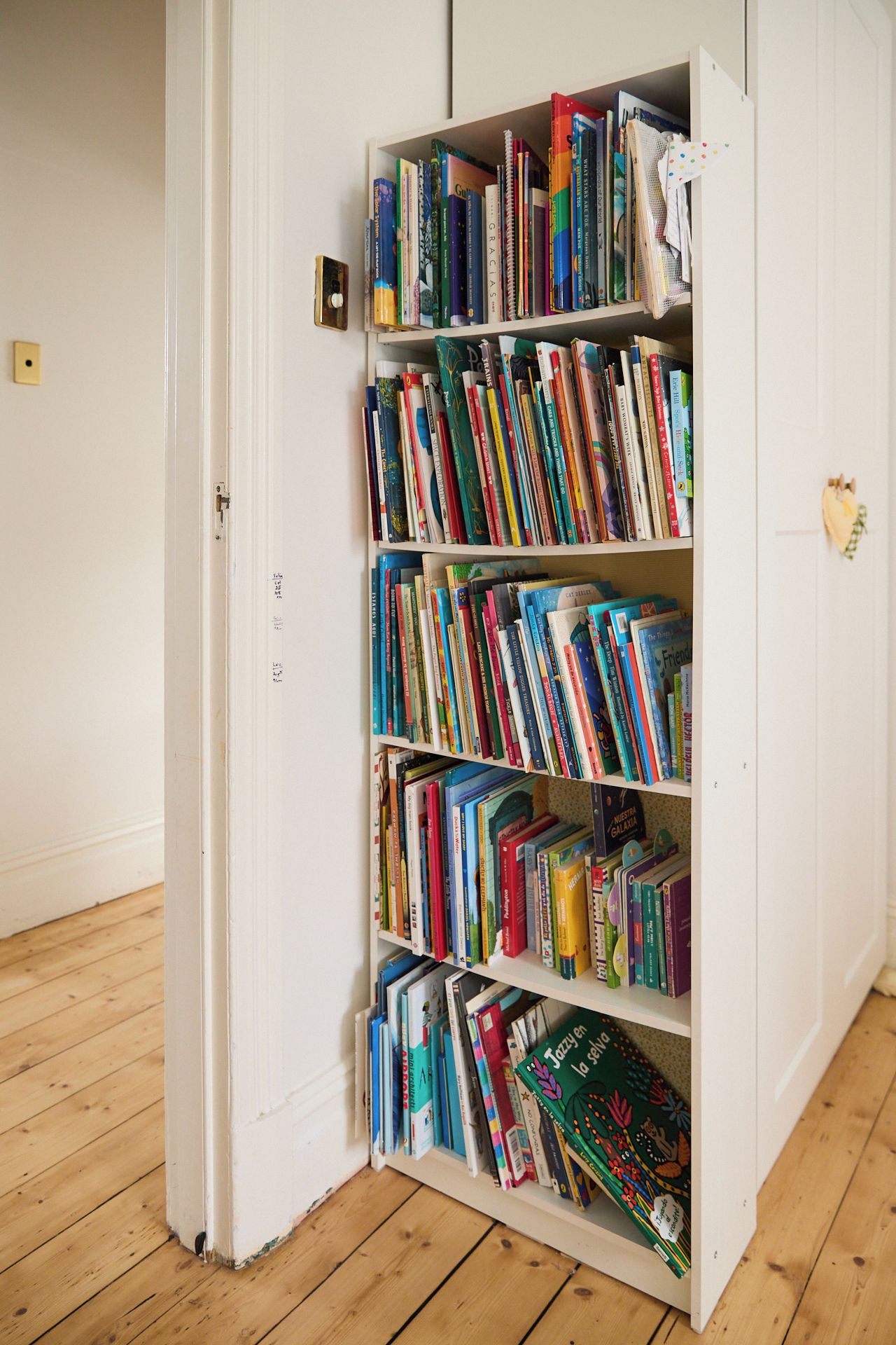 A bookshelf filled with books in a room with wooden flooring and white walls.