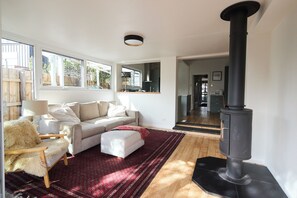 A living room with a sofa, a furry chair, a red patterned rug, and a black stove. - The Merri Creekside Living near Cafs and Culture (Northcote)