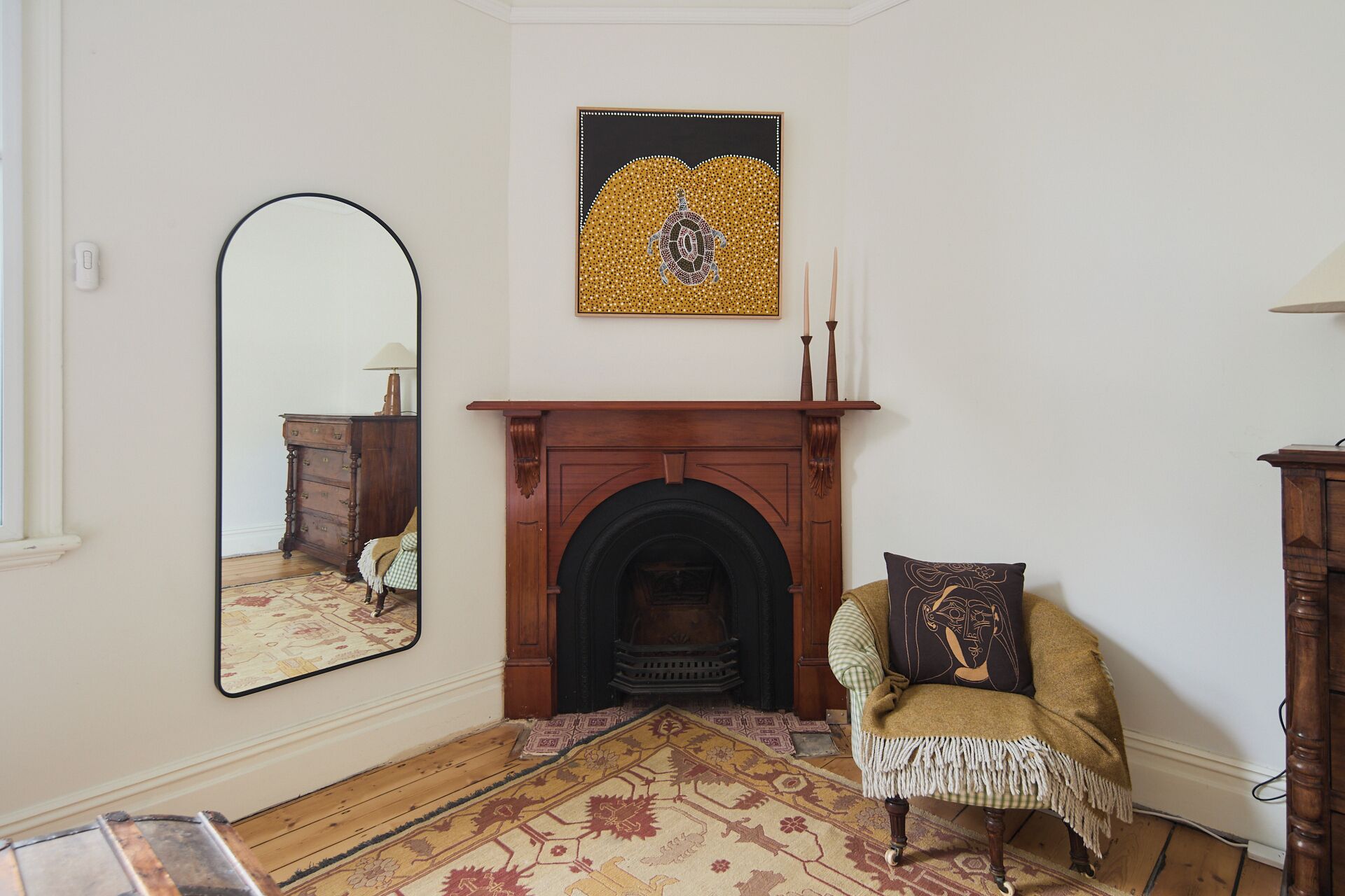 A room with a fireplace, a mirror, a chair, and a rug.