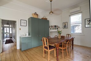 A dining area with a wooden table and chairs, a green cabinet, and a bookshelf with books. - The Merri Creekside Living near Cafs and Culture (Northcote)