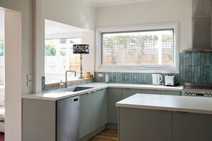 A modern kitchen with a built-in dishwasher, a window with a view of the outside, and a kettle on the counter. - The Merri Creekside Living near Cafs and Culture (Northcote)