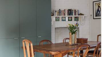 A dining area with a wooden table and chairs, a ceiling fan, and a bookshelf against a white wall.