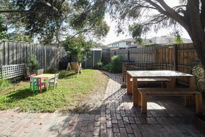 A backyard with a brick patio, wooden furniture, and a wooden fence. - The Merri Classic Victorian Home by Walking Trails (Northcote)