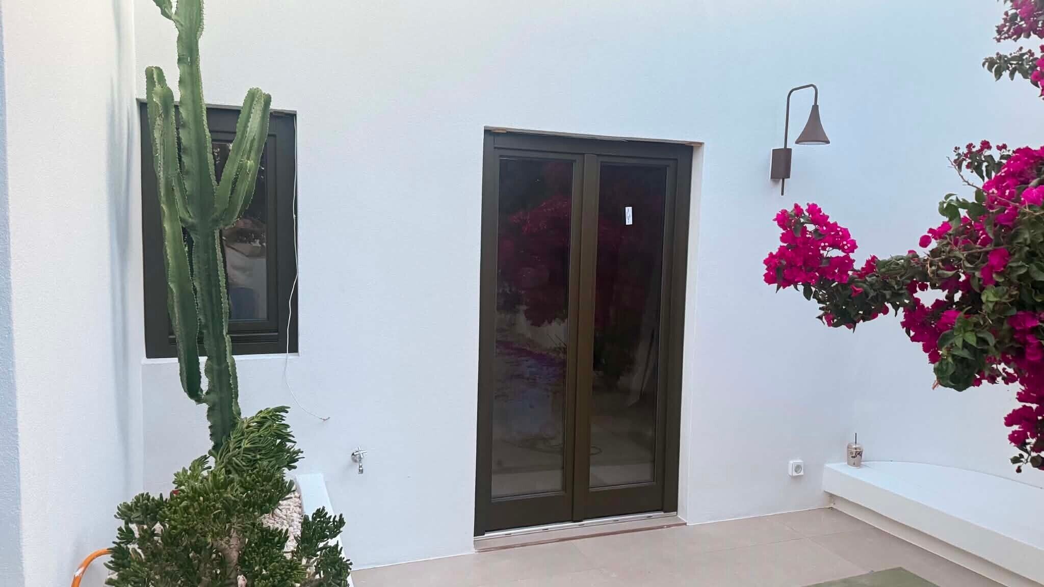 Ein modernes Gebäude mit einer Schiebetür, einem Kaktus und Bougainvillea-Blumen.