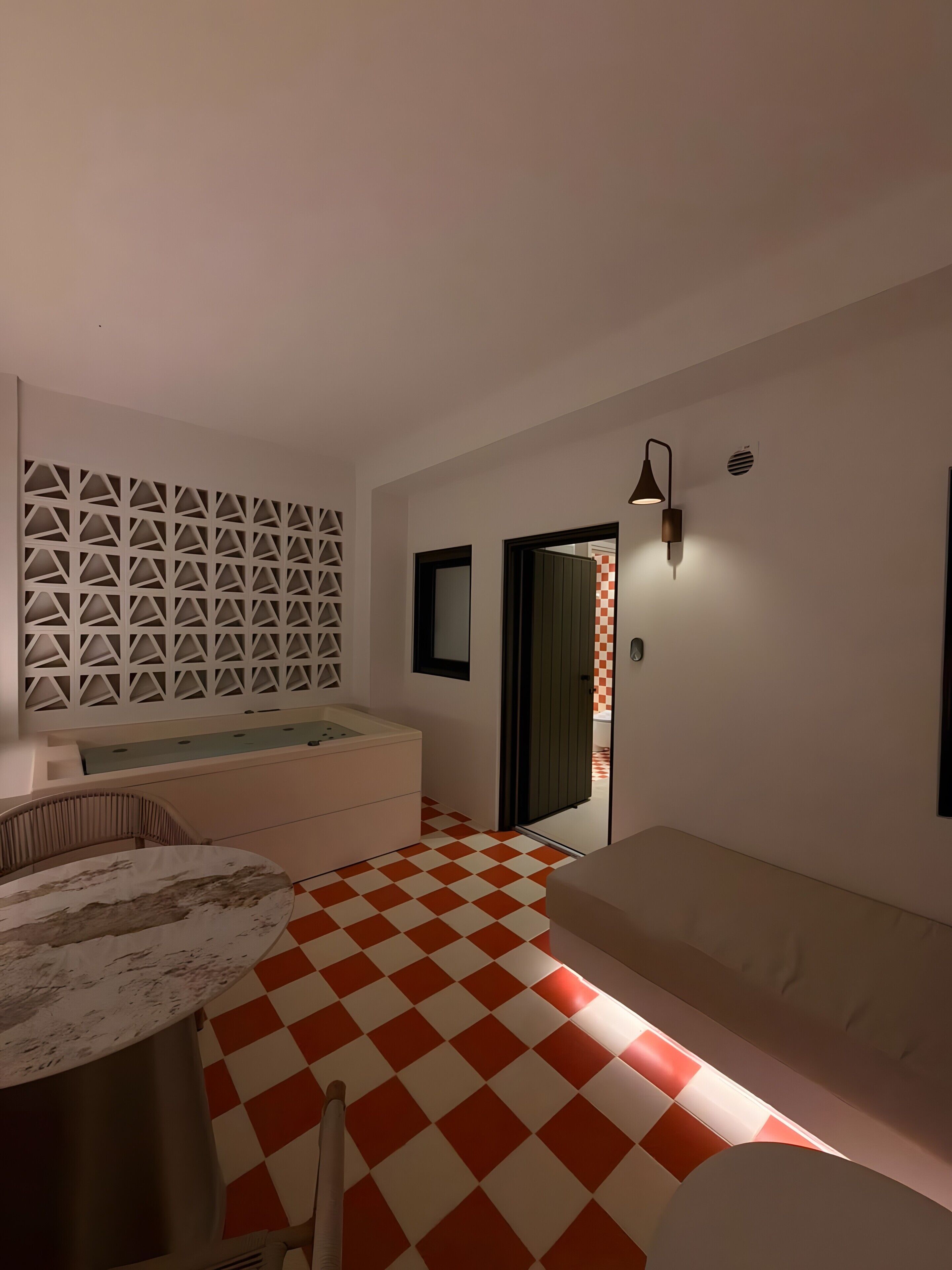 Une pièce avec un sol à carreaux, un canapé, une table et un mur orné d’un motif géométrique.
