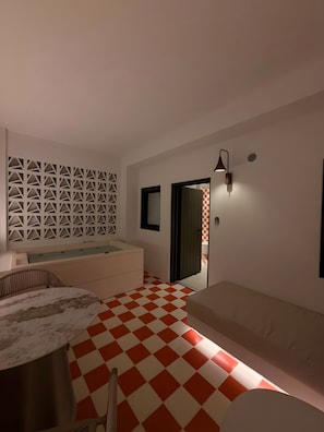 Une pièce avec un sol à carreaux, un canapé, une table et un mur orné d’un motif géométrique.
