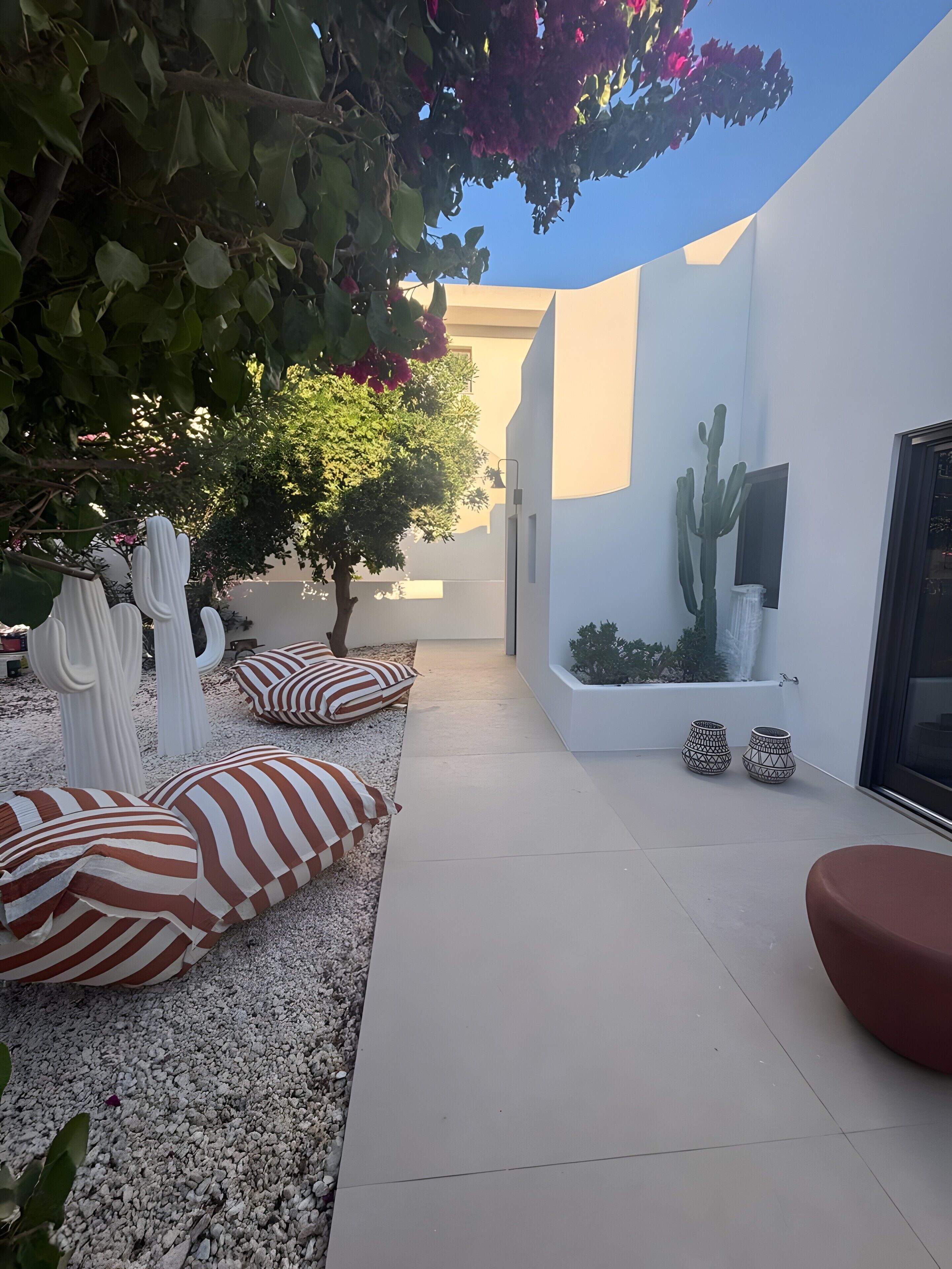 Eine moderne Terrassenanlage im Freien mit weißen Wänden, einem Kaktus und gestreiften Kissen.