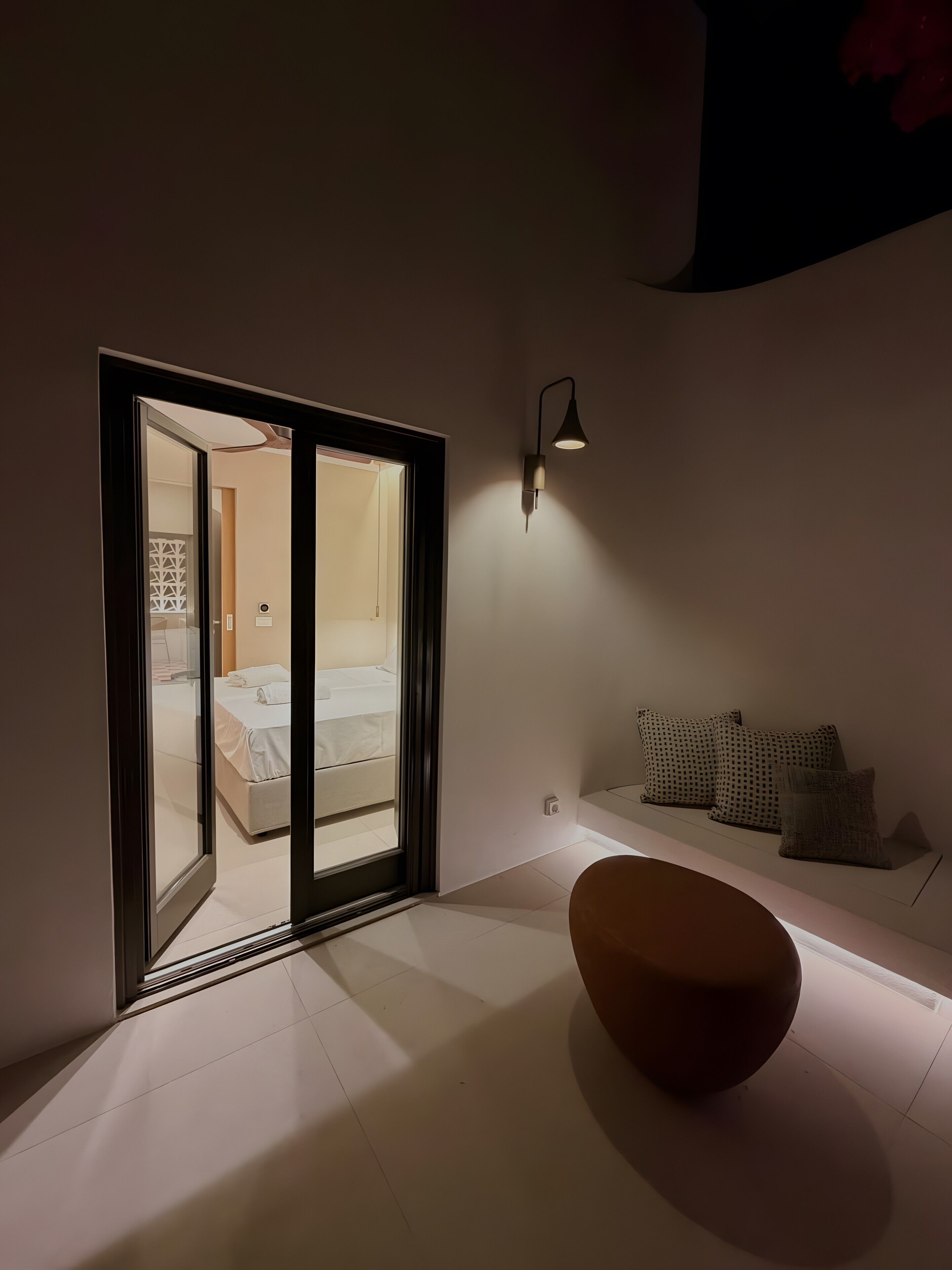 A modern room with a bed, a bench, and a wall-mounted light fixture.