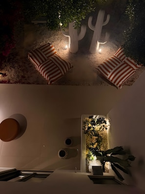 Un espace extérieur moderne, aménagé avec deux fauteuils rembourrés et un banc, le tout entouré de plantes décoratives et d’un cactus.