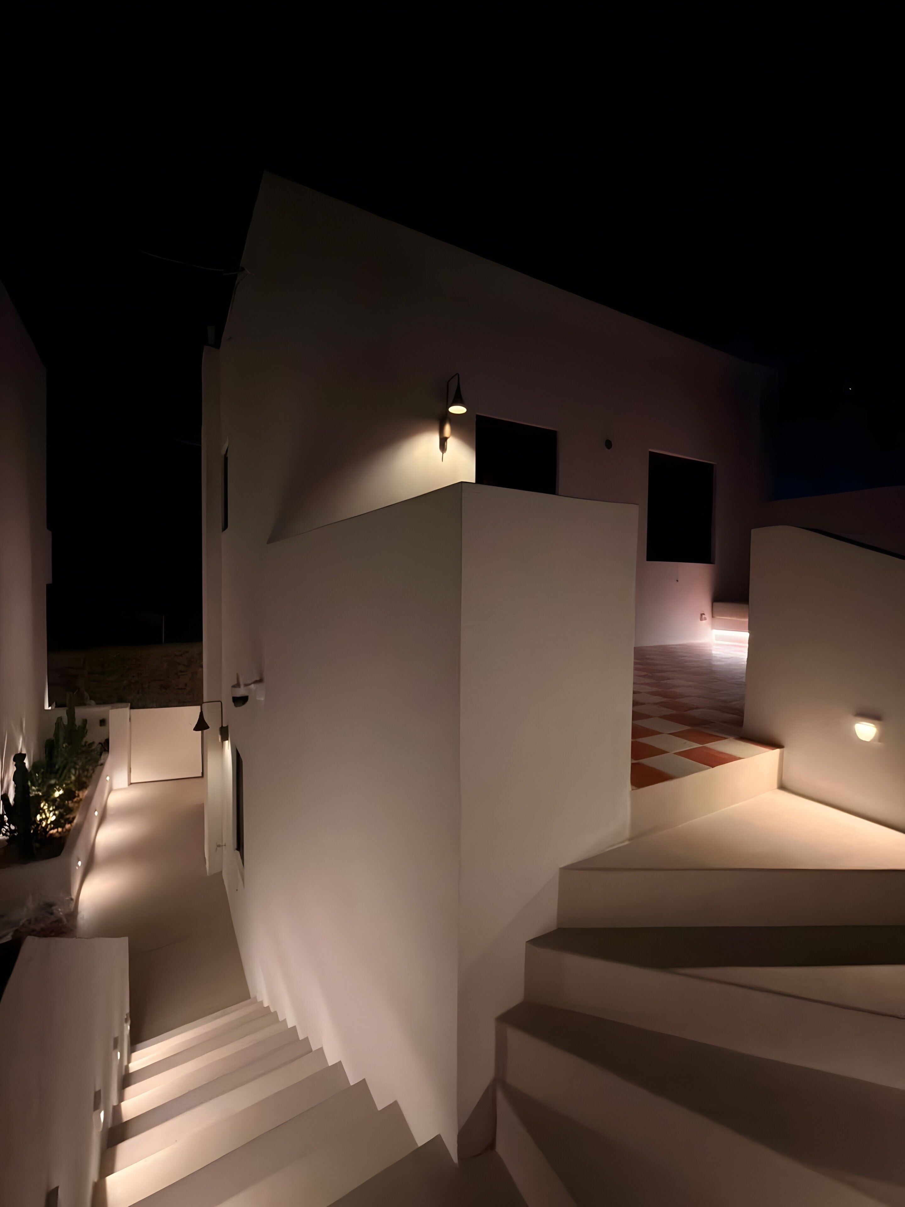 Ein modernes Gebäude mit einer Treppe, die zu einer zweiten Etage führt, einem flachen Dach und einer Lichtquelle an der Wand.