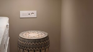 Une pièce avec un matelas blanc, une table ronde à motifs, un luminaire suspendu et une prise électrique murale.