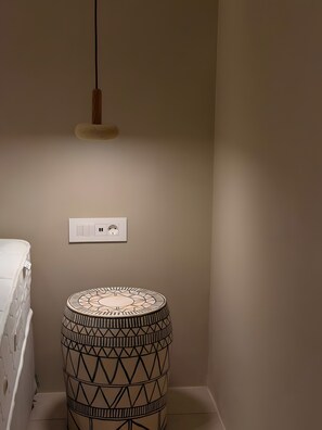 A room with a white mattress, a patterned round table, a hanging light fixture, and a wall socket.