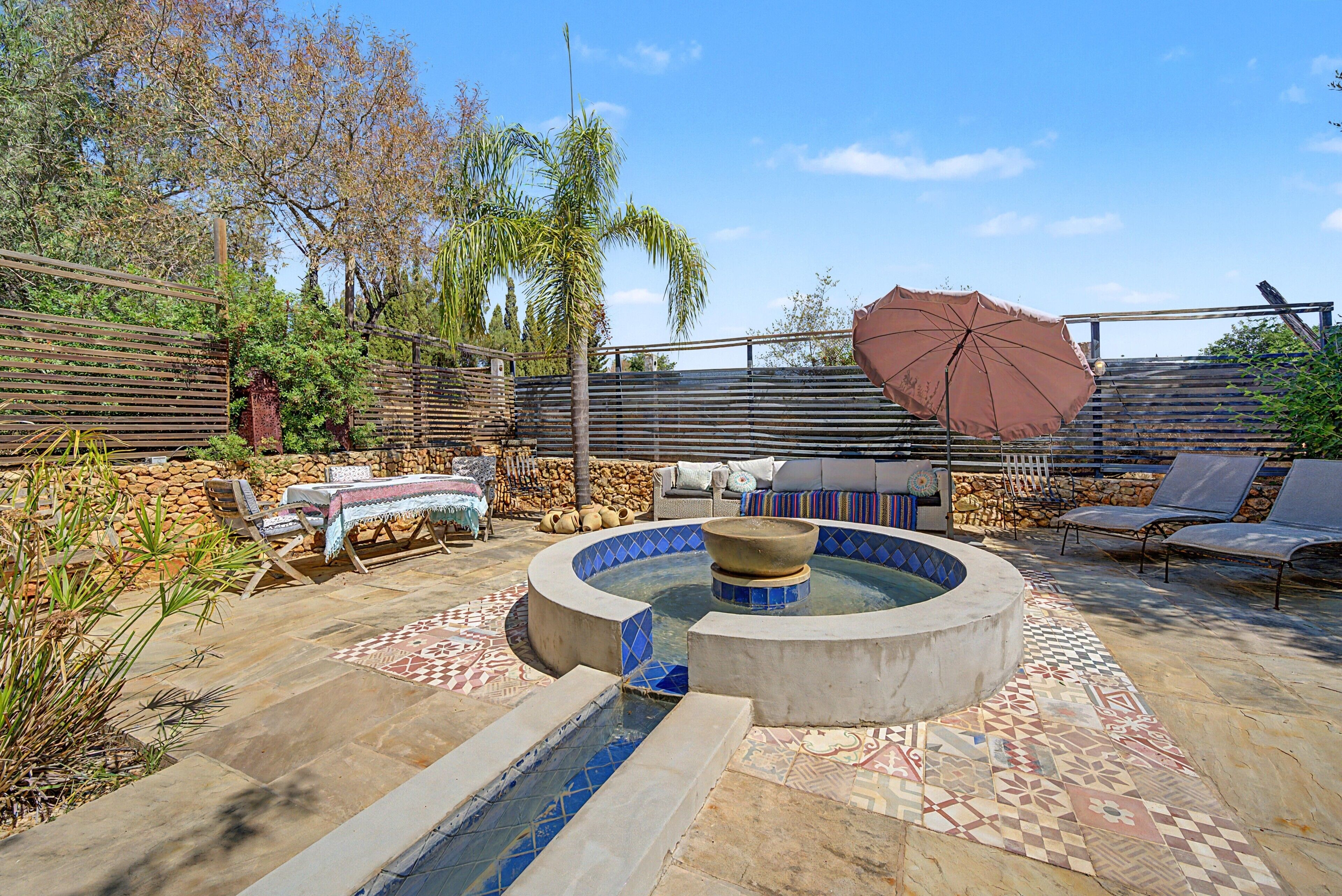 A pool area with a hot tub, lounge chairs, and a pergola with an umbrella.