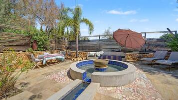 Un espace piscine comprenant un jacuzzi, des chaises longues et une pergola avec un parasol.