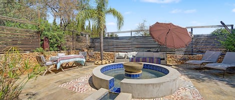 A pool area with a hot tub, lounge chairs, and a pergola with an umbrella.