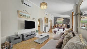 Un salon moderne avec un téléviseur à écran plat, des canapés gris, une table basse et un lustre.