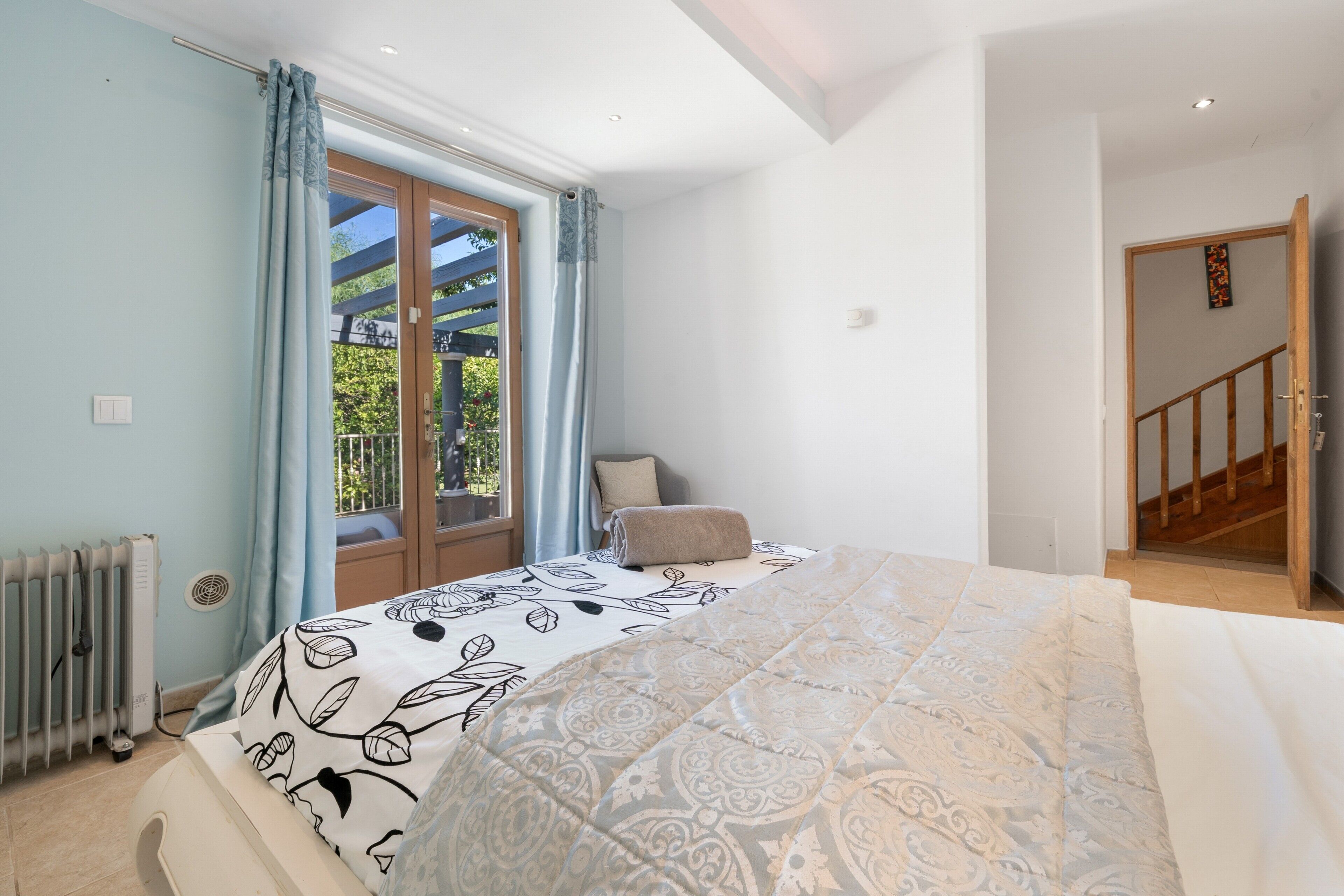 Une chambre à coucher avec un lit, un radiateur, une fenêtre avec des rideaux et une vue sur l’extérieur.