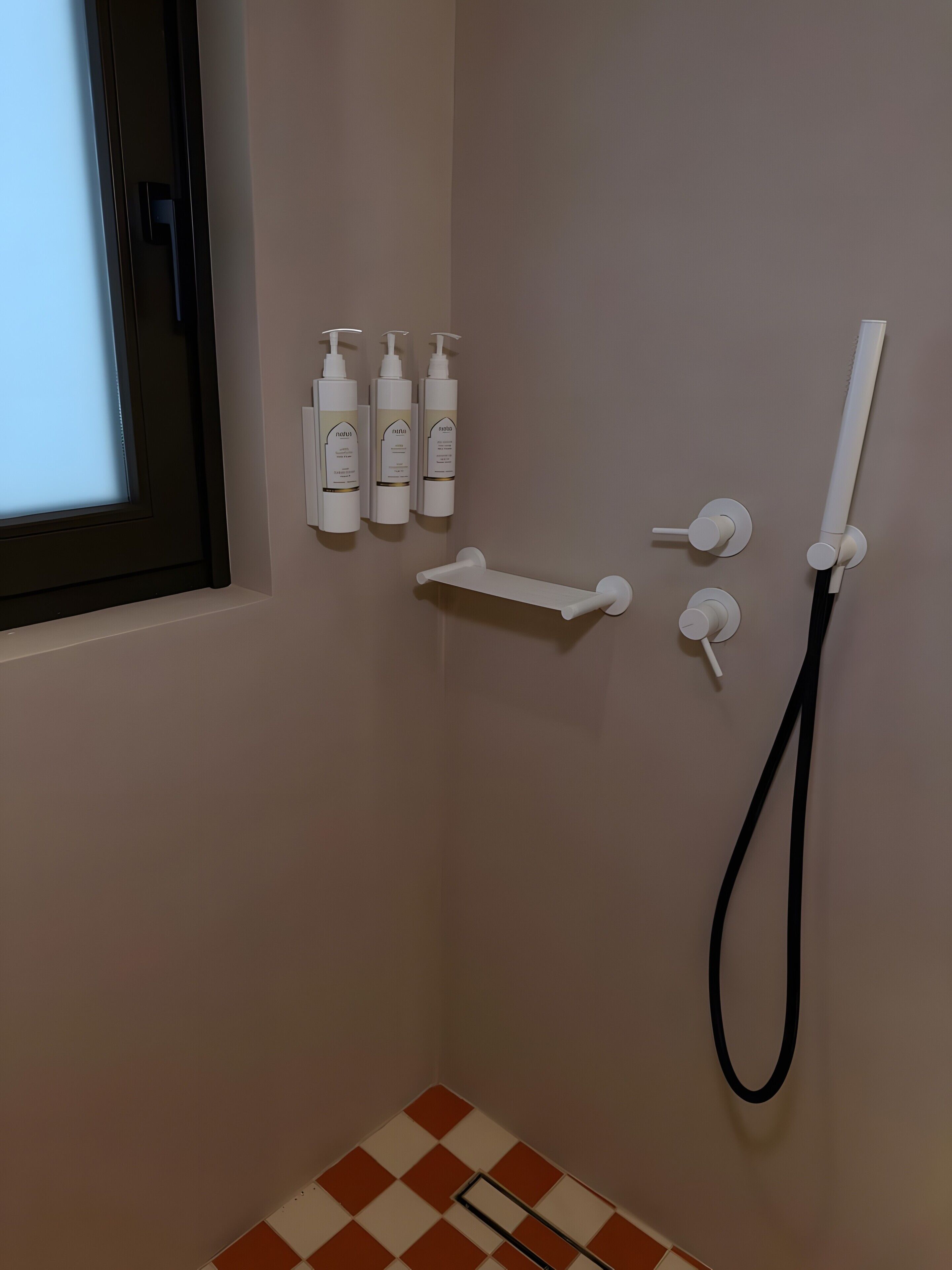Une salle de bain avec une douche, une fenêtre et trois bouteilles de shampoing accrochées au mur.