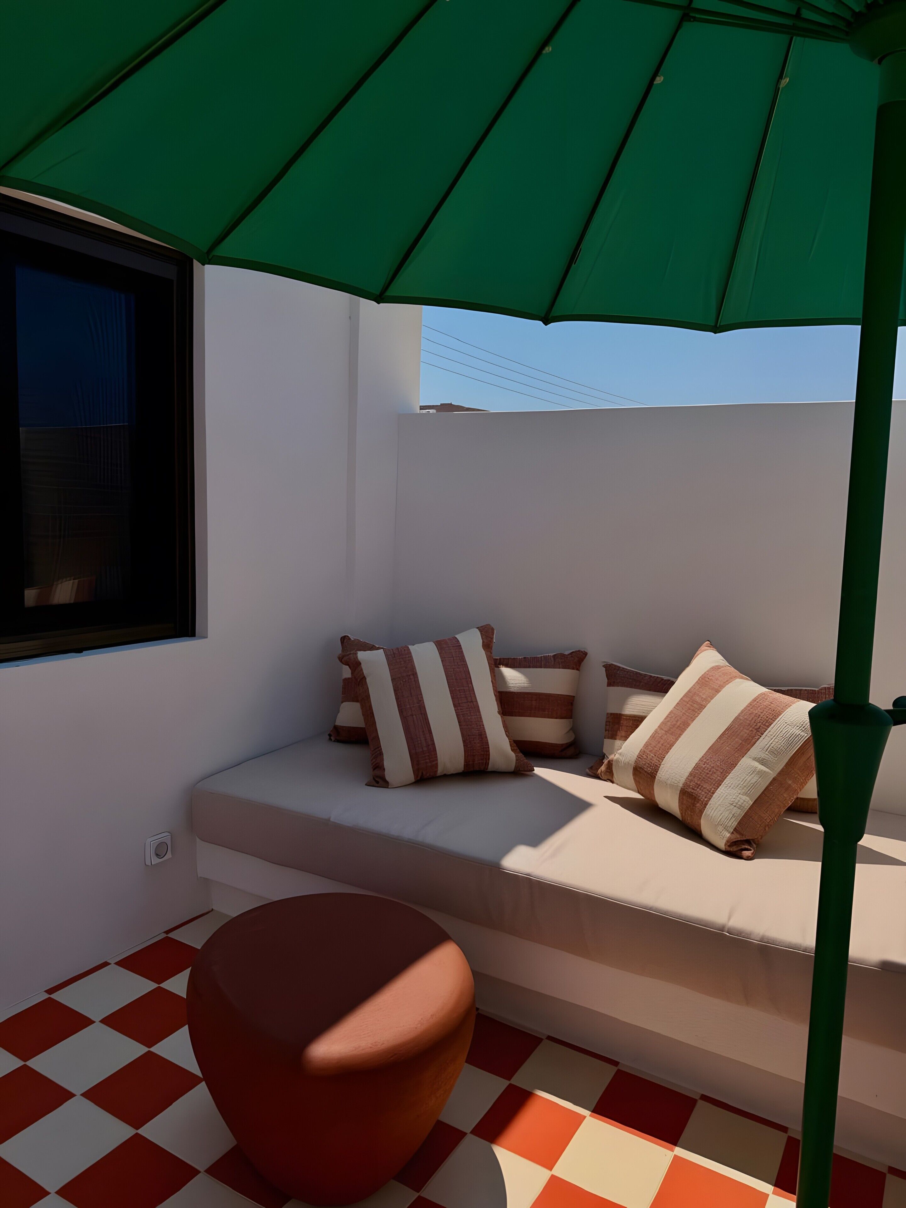 A room with a checkered floor, a sofa with striped cushions, a green umbrella, and a window.