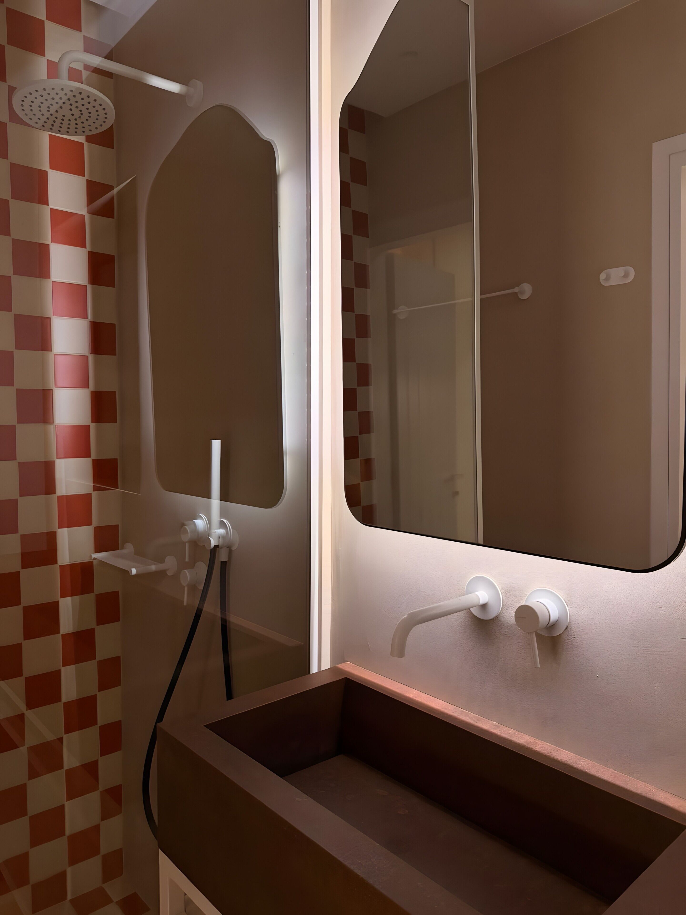Ein Badezimmer mit Schachbrettmuster an der Wand, einer Dusche, einem Waschbecken mit Spiegel und einem Handtuchhalter.