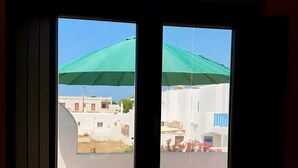 A window with a view of a residential area, including buildings and a green canopy. - Holiday Home 'Bluewaves Sunstone Terrace House' with Private Garden, Balcony and Wi-Fi (Antiparos)