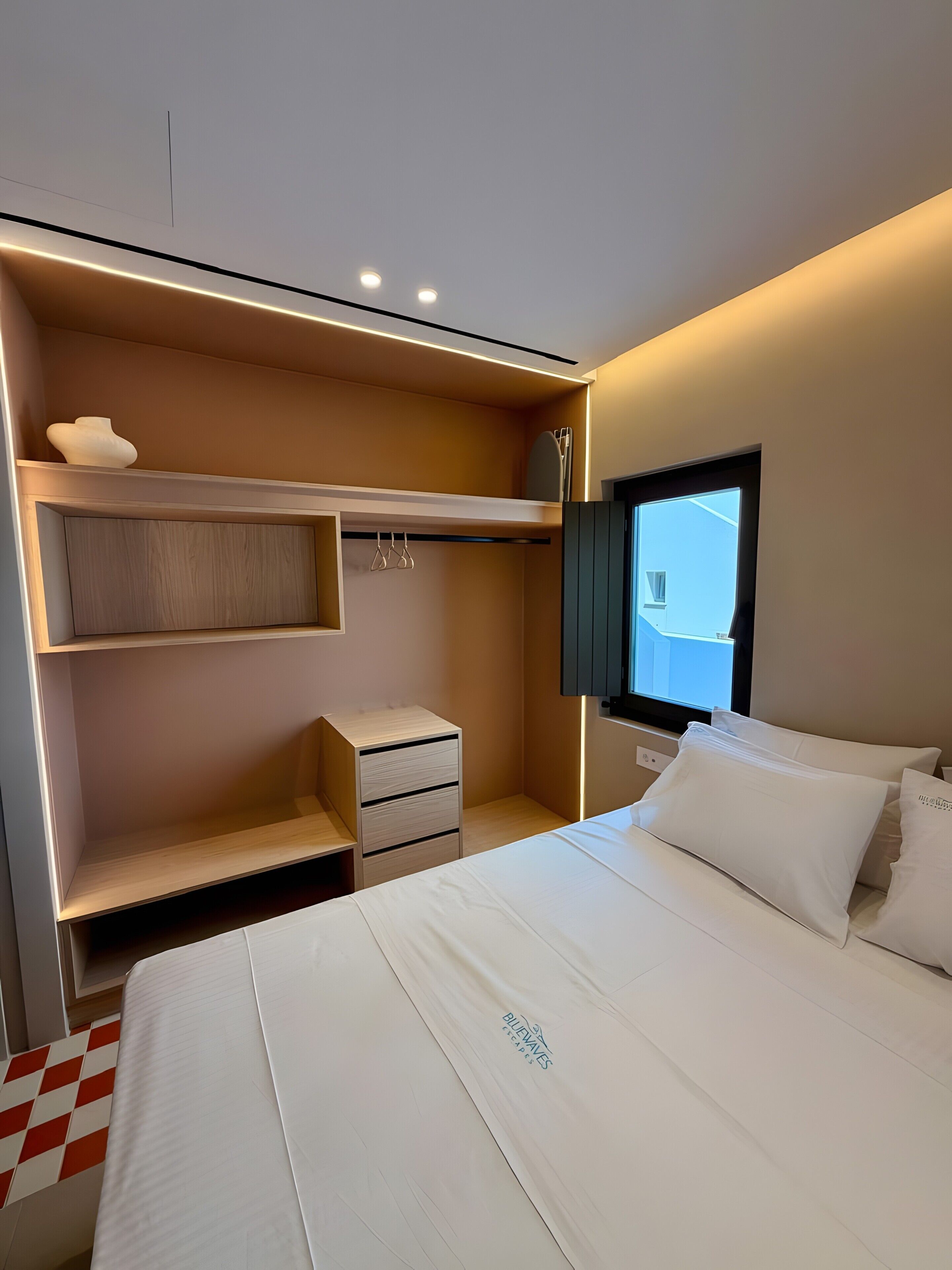 Una habitación de hotel con una cama, un armario, una mesita de noche y una ventana.
