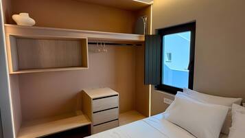 Una habitación de hotel con una cama, un armario, una mesita de noche y una ventana.
