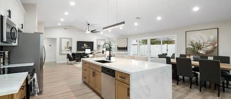 Una cocina moderna con una isla de mármol, armarios de madera y un comedor con mesa y sillas.