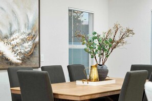 A conference room with a wooden table, grey chairs, a vase with branches, and a large abstract painting on the wall. - NEW|Desert Springs @Westgate|Designer Pool Retreat (Glendale)