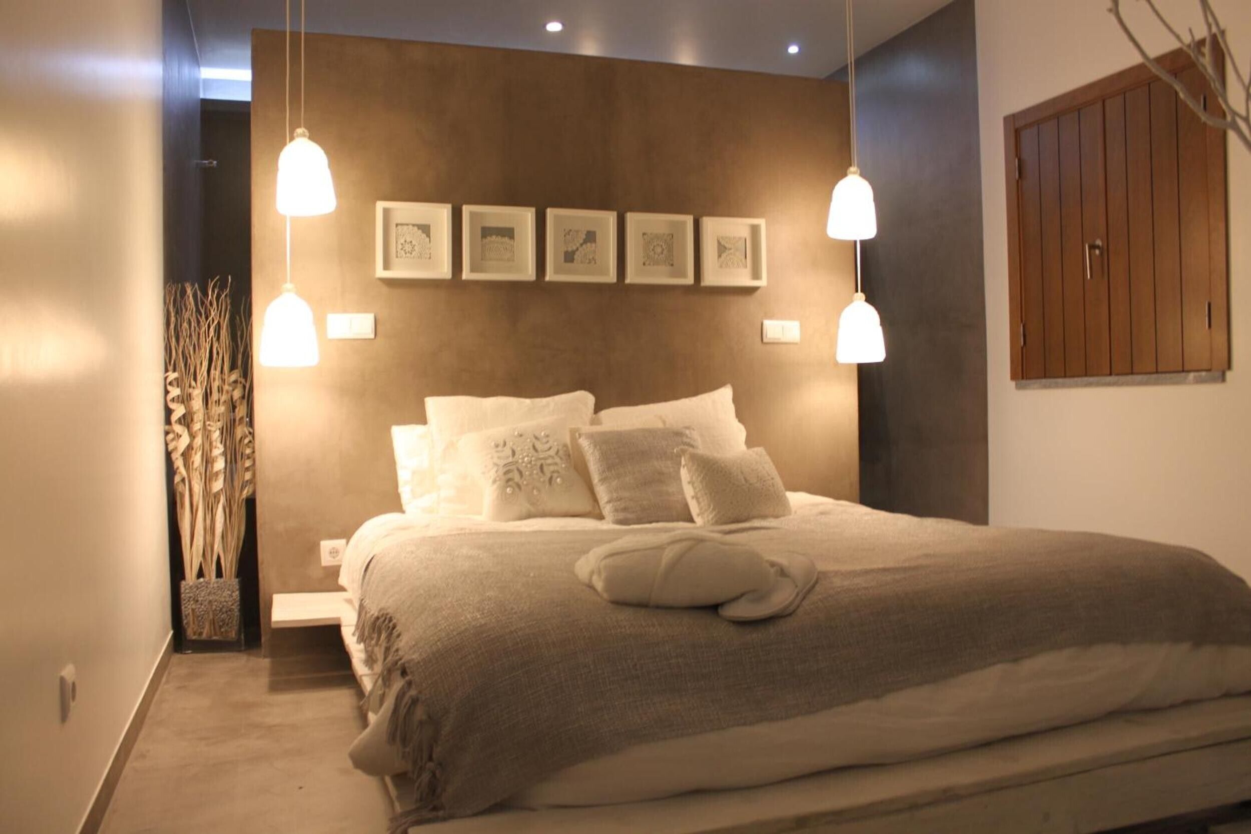 Een slaapkamer met een groot bed, twee nachtkastjes, een wandmeubel en een hanglamp.