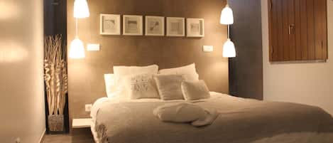 A bedroom with a large bed, two bedside tables, a nightstand, a wall-mounted wardrobe, and a hanging light fixture.