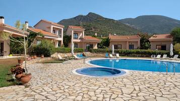 A pool area with stone flooring, lounge chairs, and a mountain backdrop.