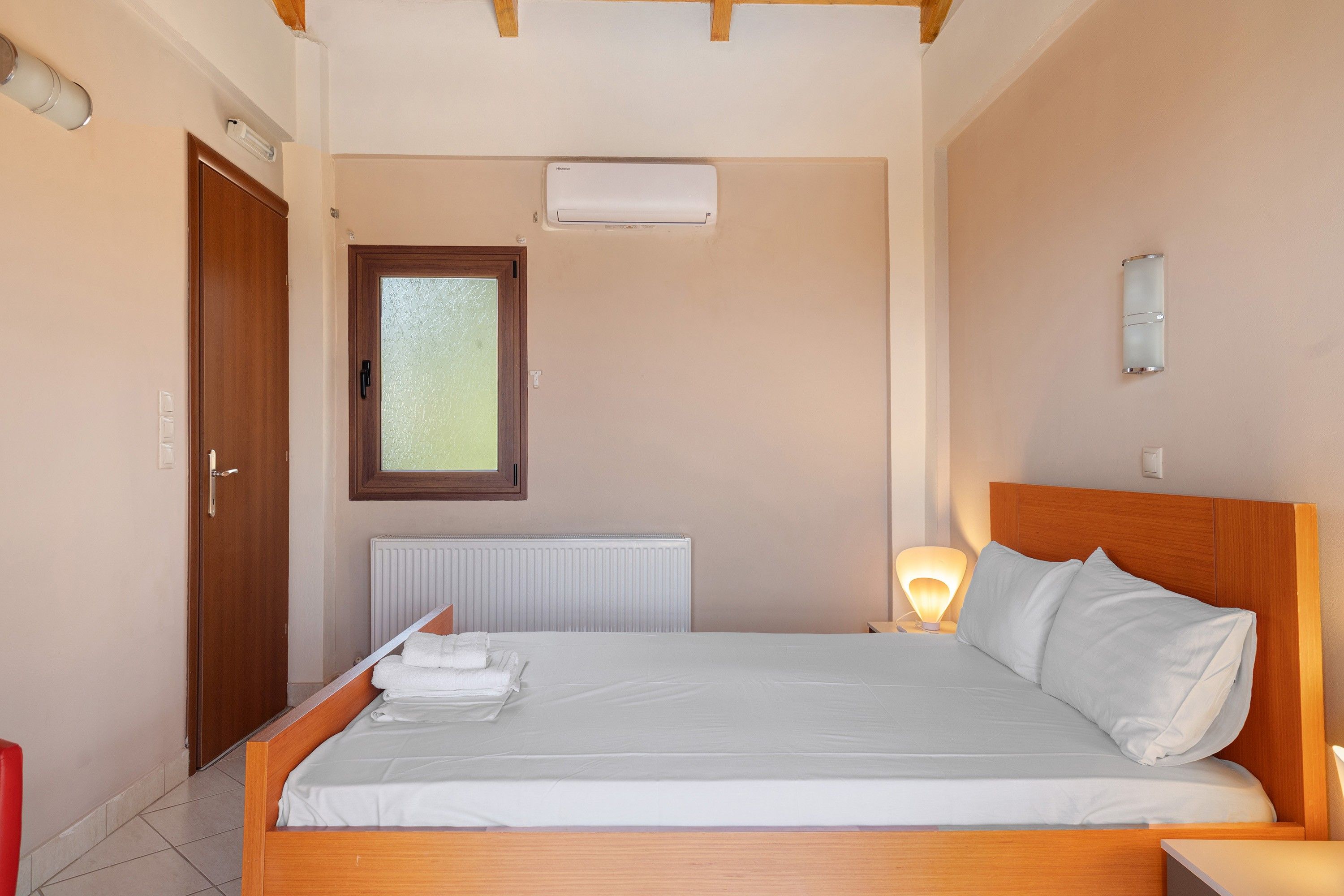 Een slaapkamer met een houten bed, een radiator, een raam en een wandlamp.