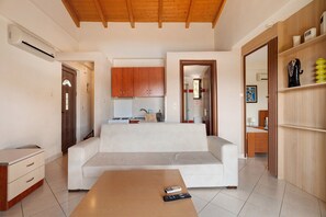 A modern living room with a sofa, a coffee table, and a kitchen area in the background. - Villa 'Fedra' with Balcony and Air Conditioning (Marathiás)