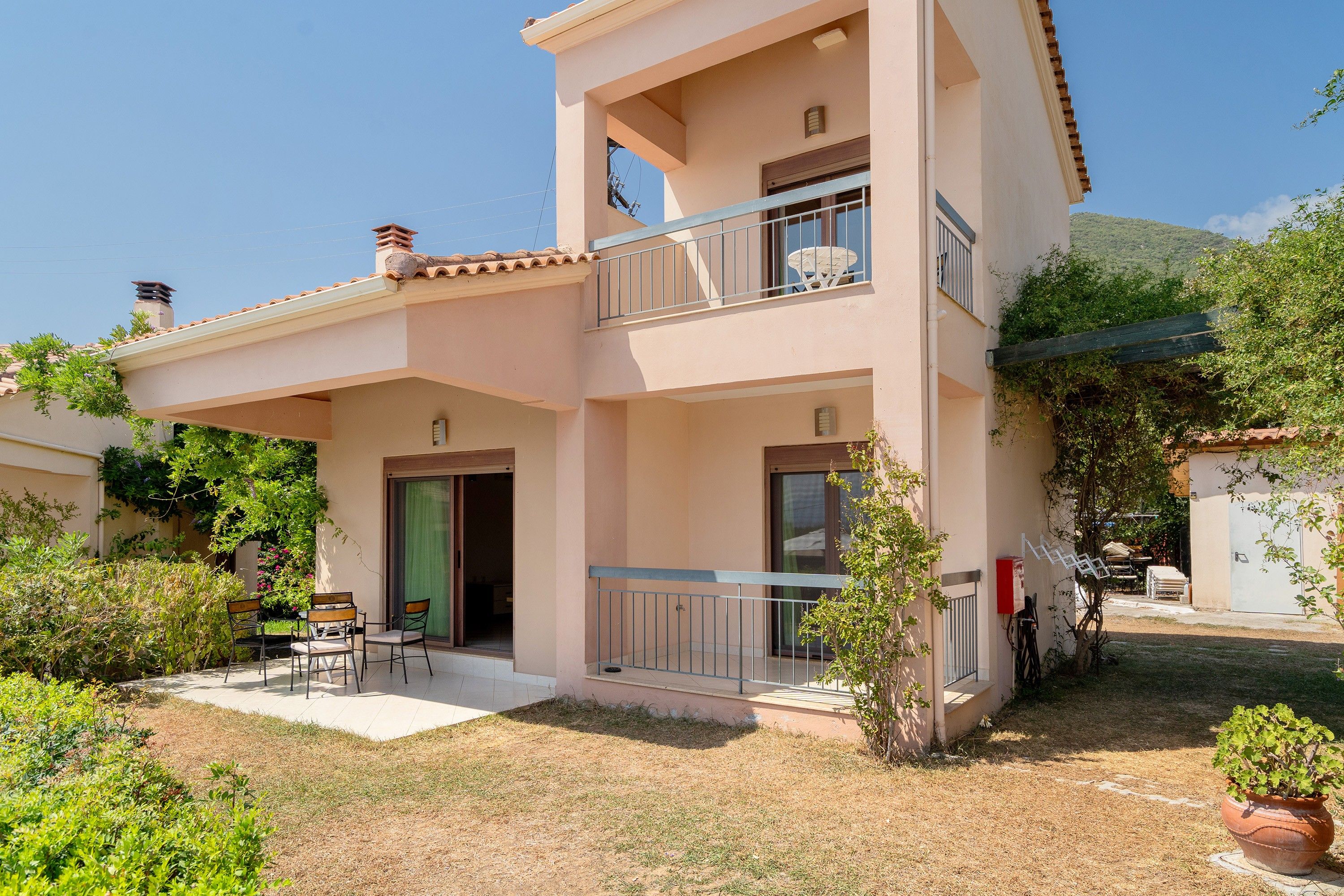 A two-story building with a balcony, a door, and a small patio area with chairs.