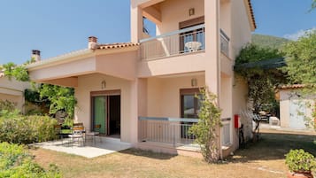A two-story building with a balcony, a door, and a small patio area with chairs.