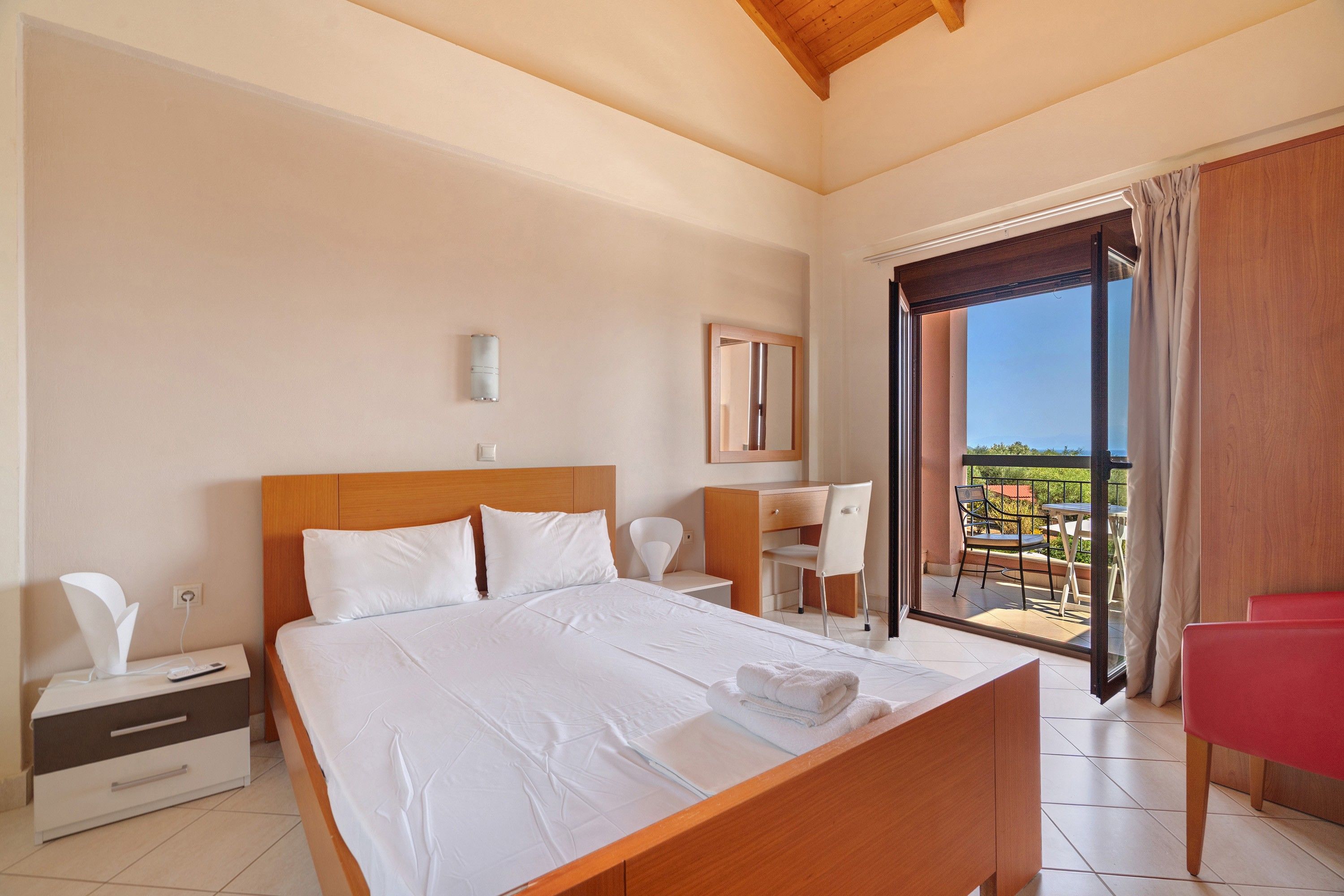 A hotel room with a bed, a desk, a chair, and a balcony with a view.